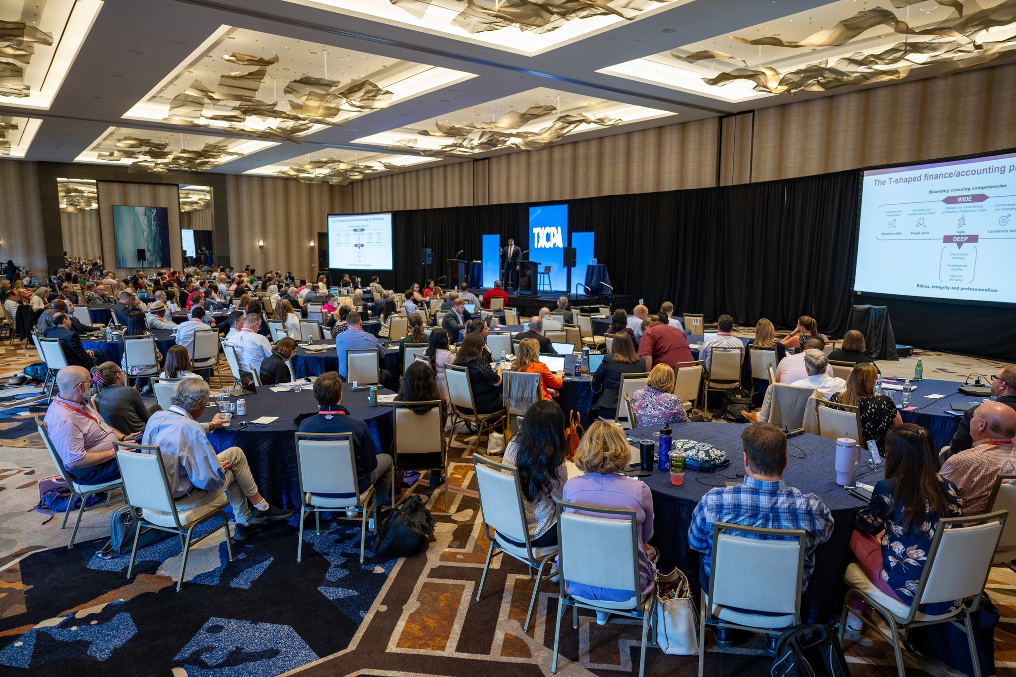 Audience seated at round tables watching a speaker on stage during the TXCPA conference