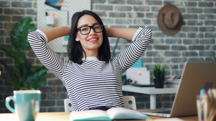Smiling woman leaning back at her desk in a casual, creative workspace